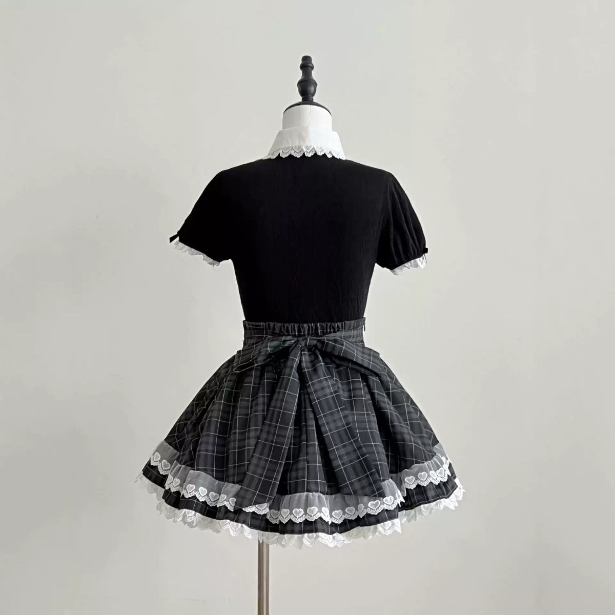 Back view of the Lolita dress, showing black puff sleeves, a checked waist bow, and white lace around the hem.