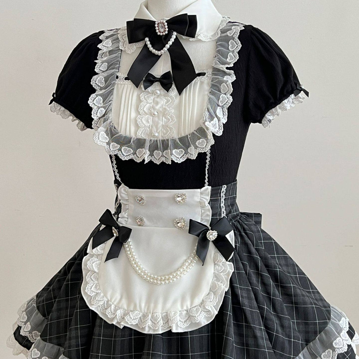 Angled close-up of the Lolita dress, showing its heart-patterned lace bodice, white apron, and pearl-look waist chains.