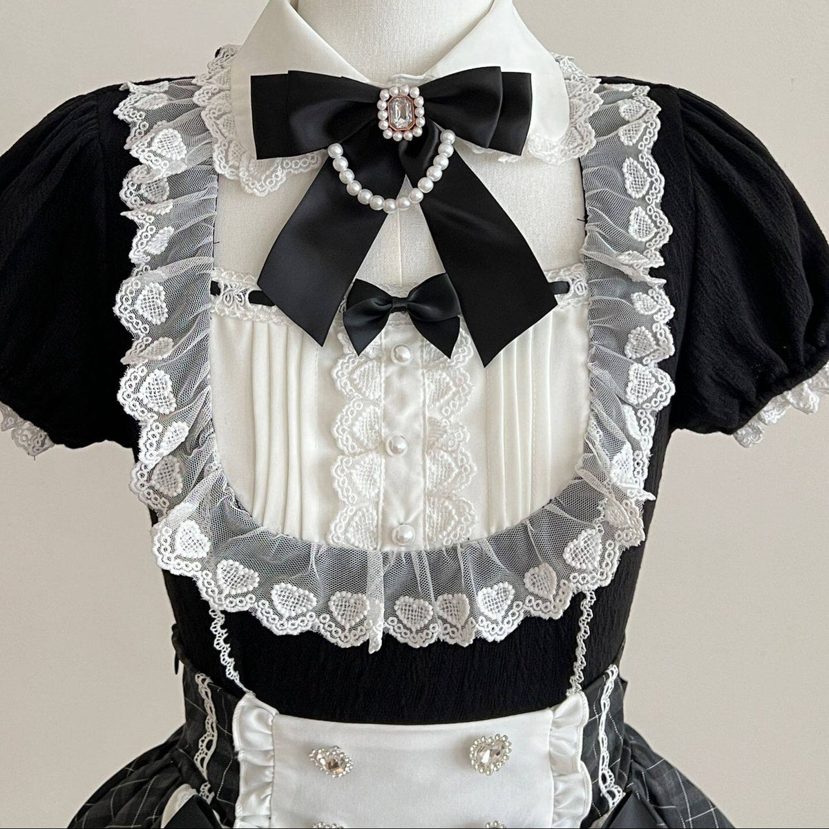 Close-up of the dress neckline with a white collar, black bow, pearl-look accents, and heart-patterned lace.
