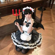A model wearing the black and white Lolita dress, styled with devil horns, bat wings, and a red trident.