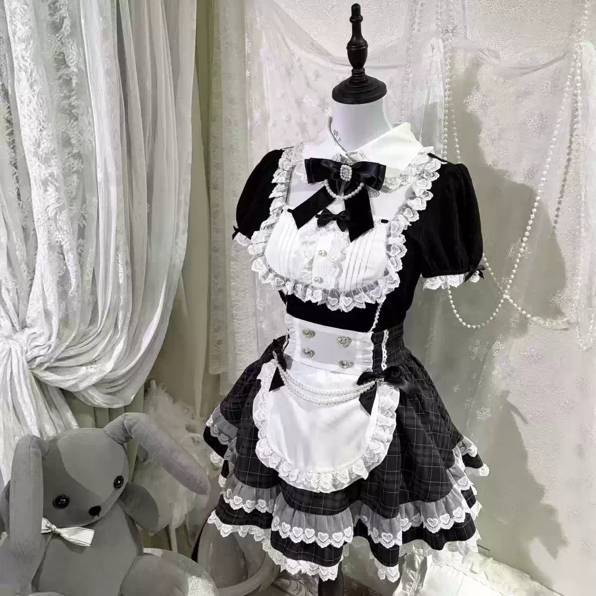 Angled mannequin view of the black and white Lolita dress with bow accents, a white apron, and a lace-trimmed checked skirt.