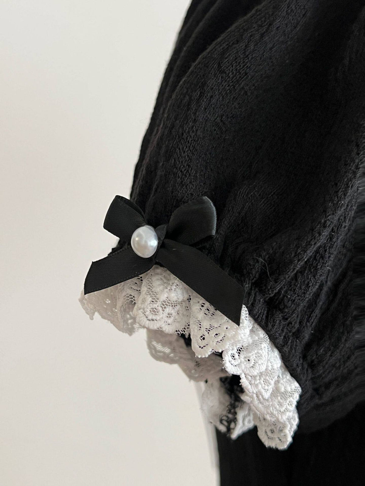 Close-up of a black puff sleeve with white lace trim and a small black bow with a pearl-look center.