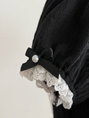 Close-up of a black puff sleeve with white lace trim and a small black bow with a pearl-look center.